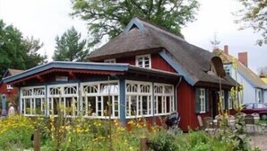 Une maison traditionnelle en briques rouges, avec un toit de chaume et des fenêtres à cadre blanc.