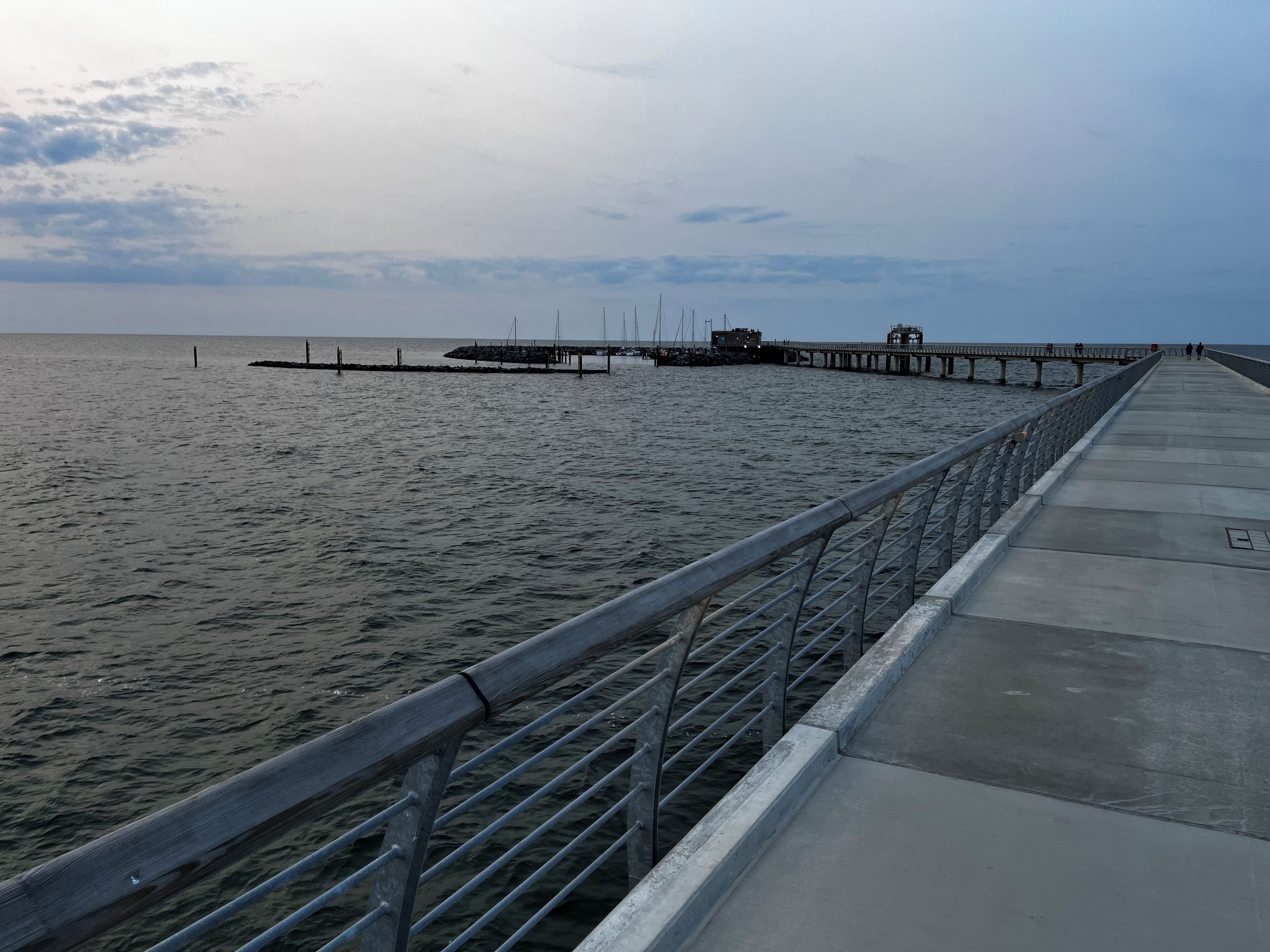 A long pier extending into calm waters with a metal railing and a concrete walkway.