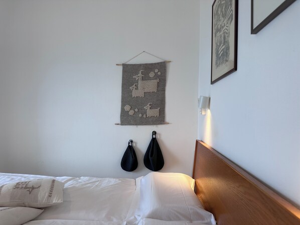 A neatly made bed with white linens, a wooden headboard, and a wall-mounted tapestry.