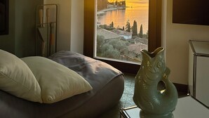Ein Zimmer mit Blick auf einen Sonnenuntergang über dem Wasser, mit einer Couch, einer Vase und einem Fernseher an der Wand.
