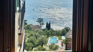 Blick durch ein Fenster auf ein Gebäude mit Pool, Grünflächen und ein Gewässer mit Booten.