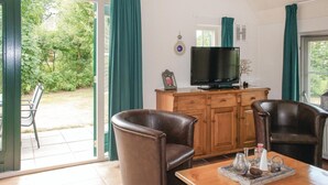 A room with a wooden cabinet, a television, two leather chairs, a table with decorative items, and a view of greenery outside. - Stunning home in Den Ham with WiFi (Den Ham)