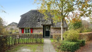 A traditional brick house with a thatched roof, a paved pathway leading to the entrance, and a small garden area with hedges and trees. - Stunning home in Den Ham with WiFi (Den Ham)