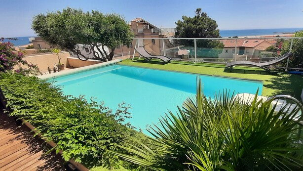 A swimming pool with a view of the sea, surrounded by greenery and a wooden deck. - * All comforts, private swimming pool, full sea view * (Fleury)