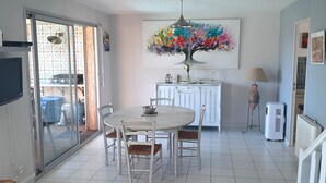 A dining area with a round table and chairs, a TV mounted on the wall, and a colorful abstract painting above the cabinets. - * All comforts, private swimming pool, full sea view * (Fleury)