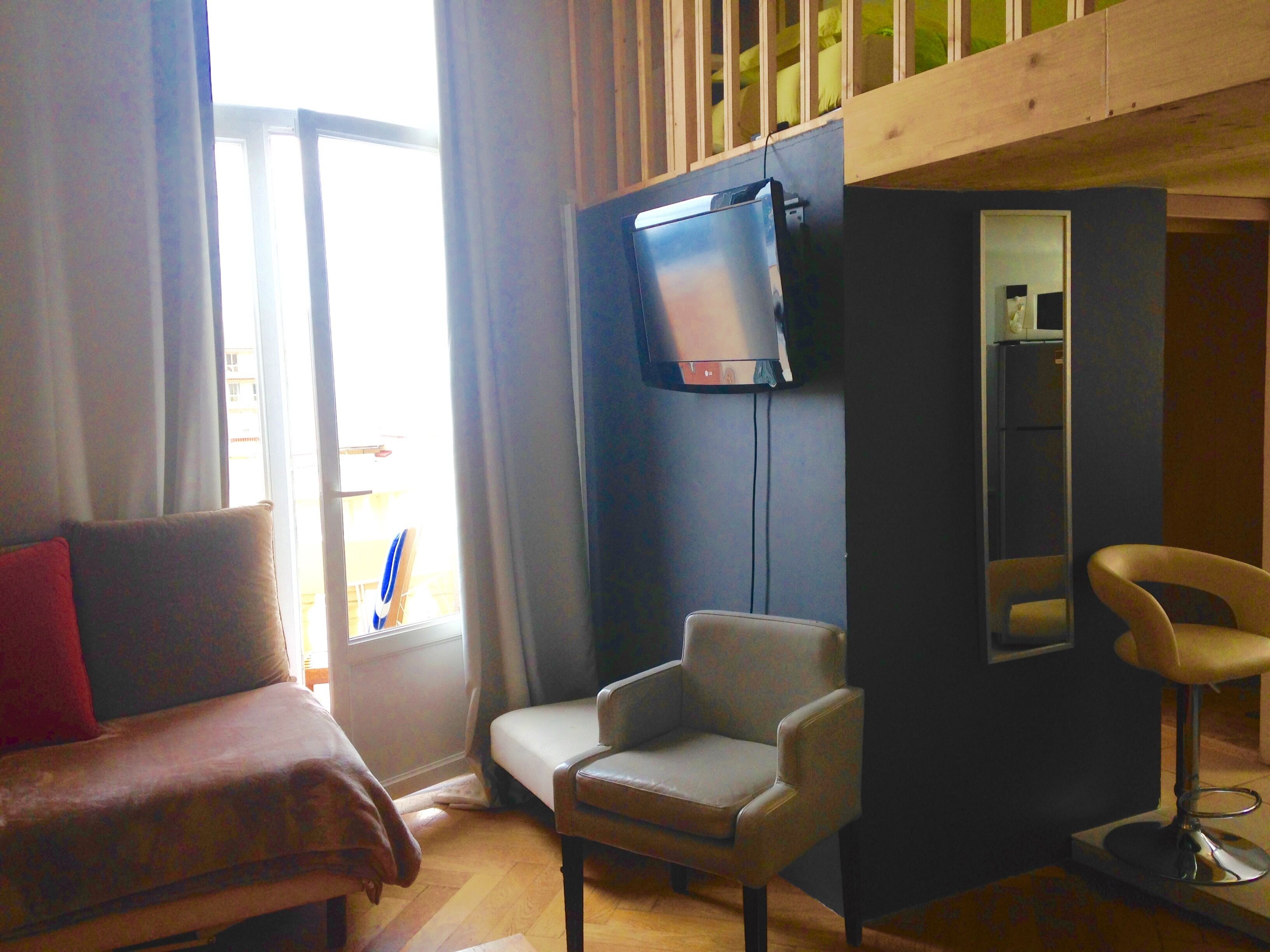Een kamer met een bank, twee fauteuils, een aan de muur bevestigde televisie en een spiegel.