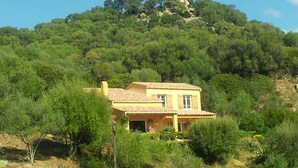 A two-story house with a tiled roof, surrounded by dense greenery and a hill in the background. - CHARMING VILLA,UP-MARKET,PANORAMIC SEA VIEW, 3MN WALK TO A BEAUTIFUL SAND BEACH (Casaglione)