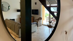 A living room with a sofa, a television, and a staircase leading to an outdoor area with a table and chairs. - CHARMING VILLA,UP-MARKET,PANORAMIC SEA VIEW, 3MN WALK TO A BEAUTIFUL SAND BEACH (Casaglione)