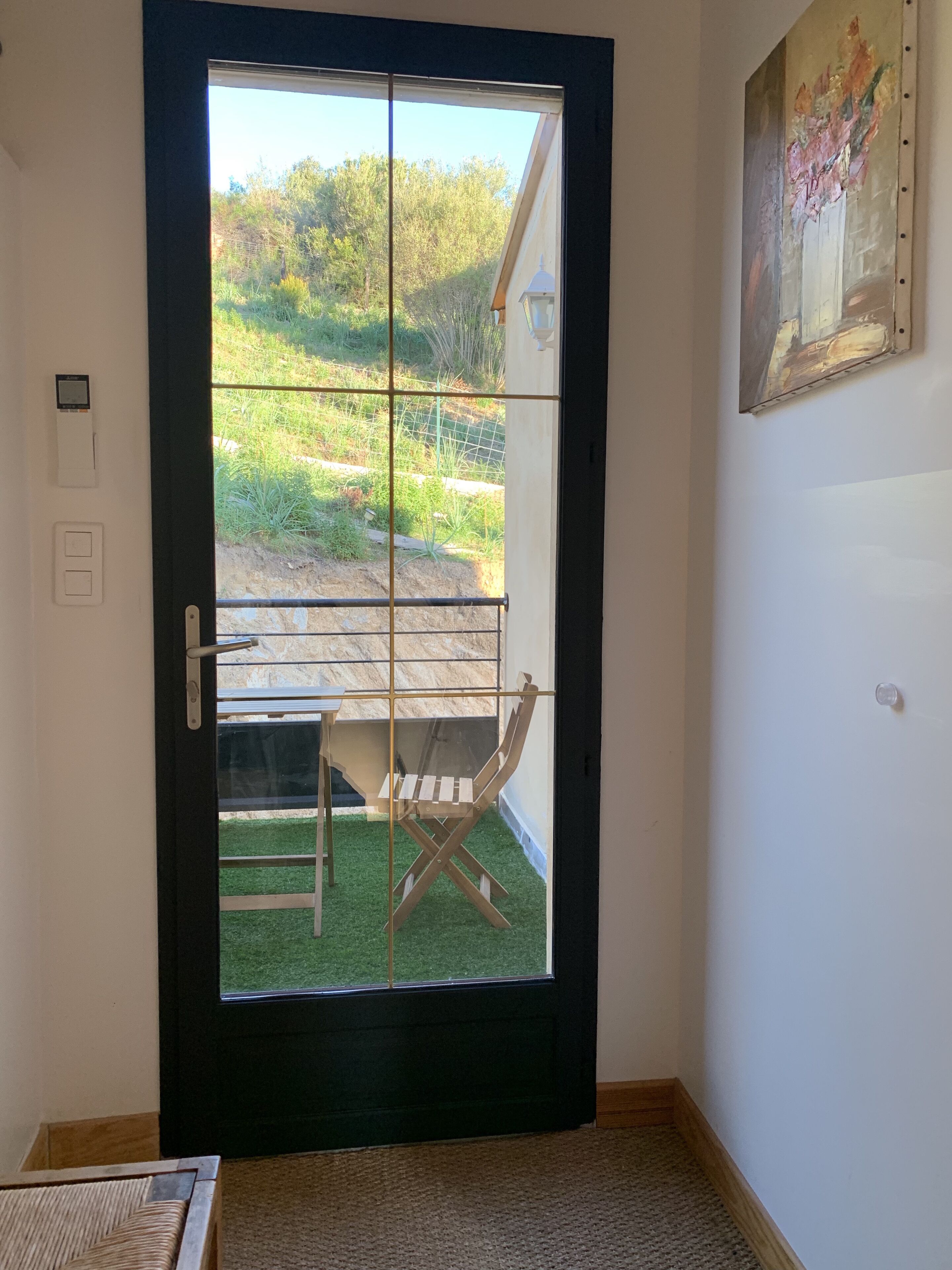 Una stanza con un'ampia porta in vetro che dà su un balcone con una sedia e un tavolo di legno.