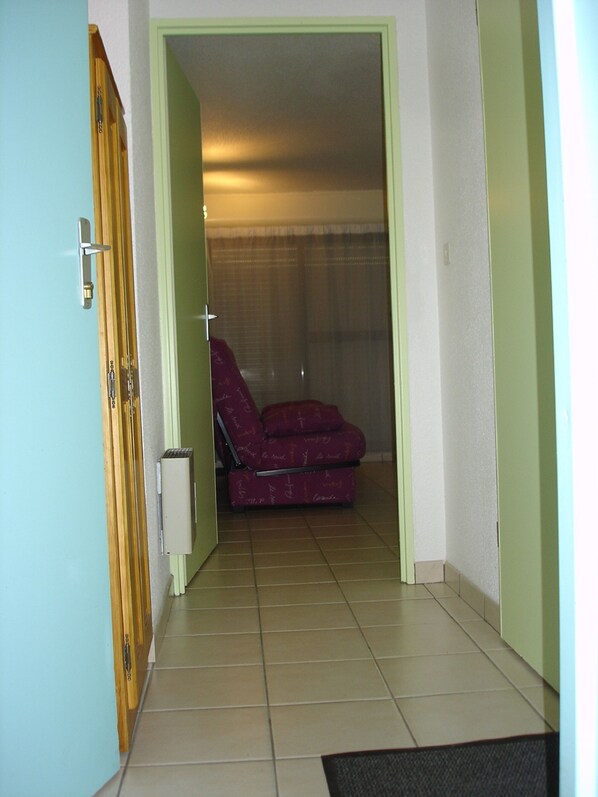 A room with a red chair, a wooden door, and a tiled floor.