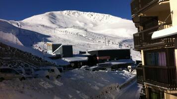 Une montagne enneigée avec un télésiège, un bâtiment avec une enseigne et un parking avec des voitures.