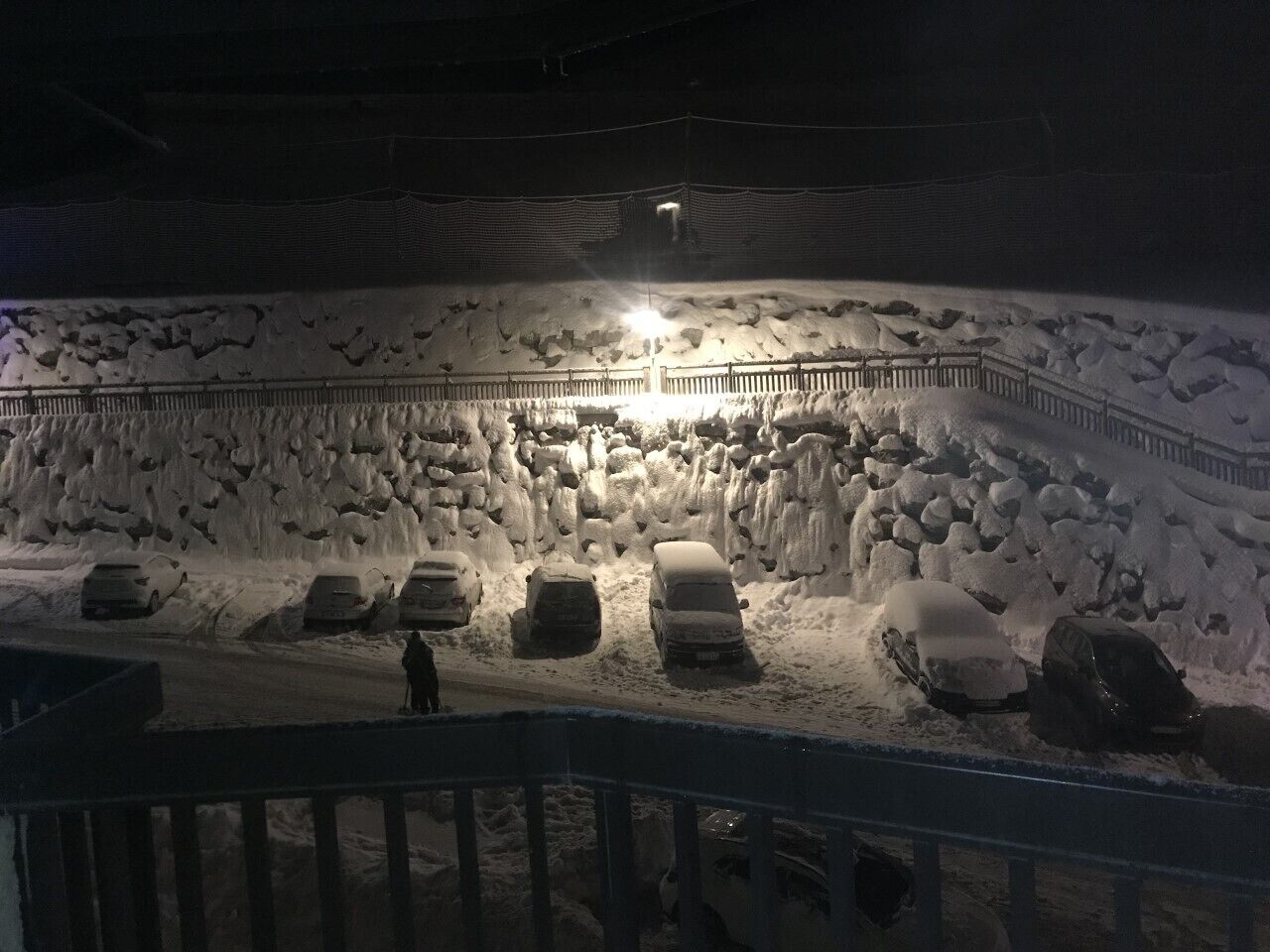 Een besneeuwd gebied met geparkeerde auto's en een persoon.