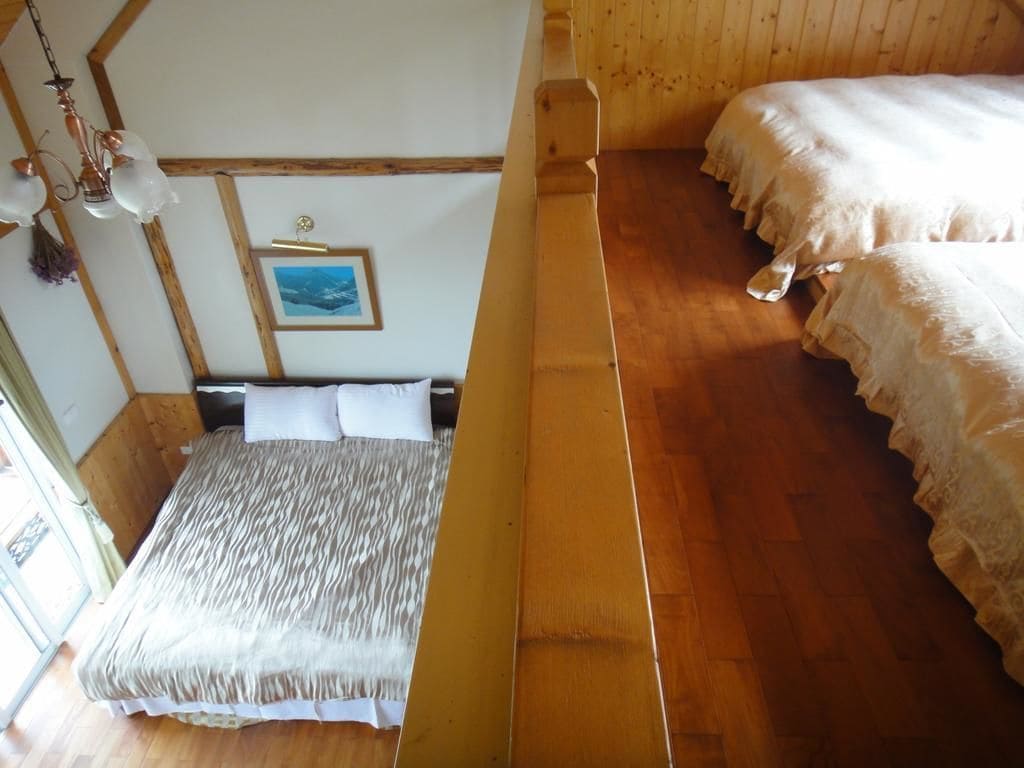 A room with a wooden floor, a bed with white bedding, a wooden headboard, a picture on the wall, and a hanging light fixture.