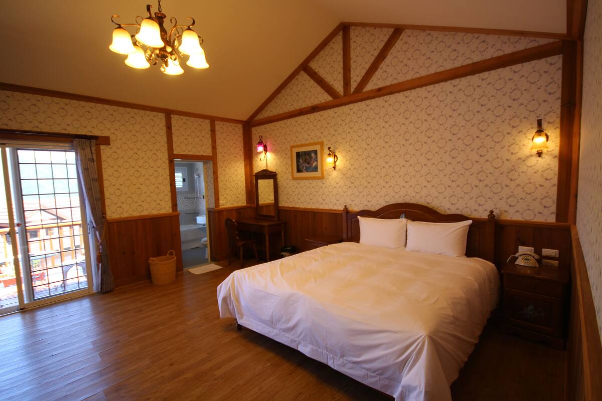 Un dormitorio con una cama grande, piso de madera, un candelabro y techo de madera.