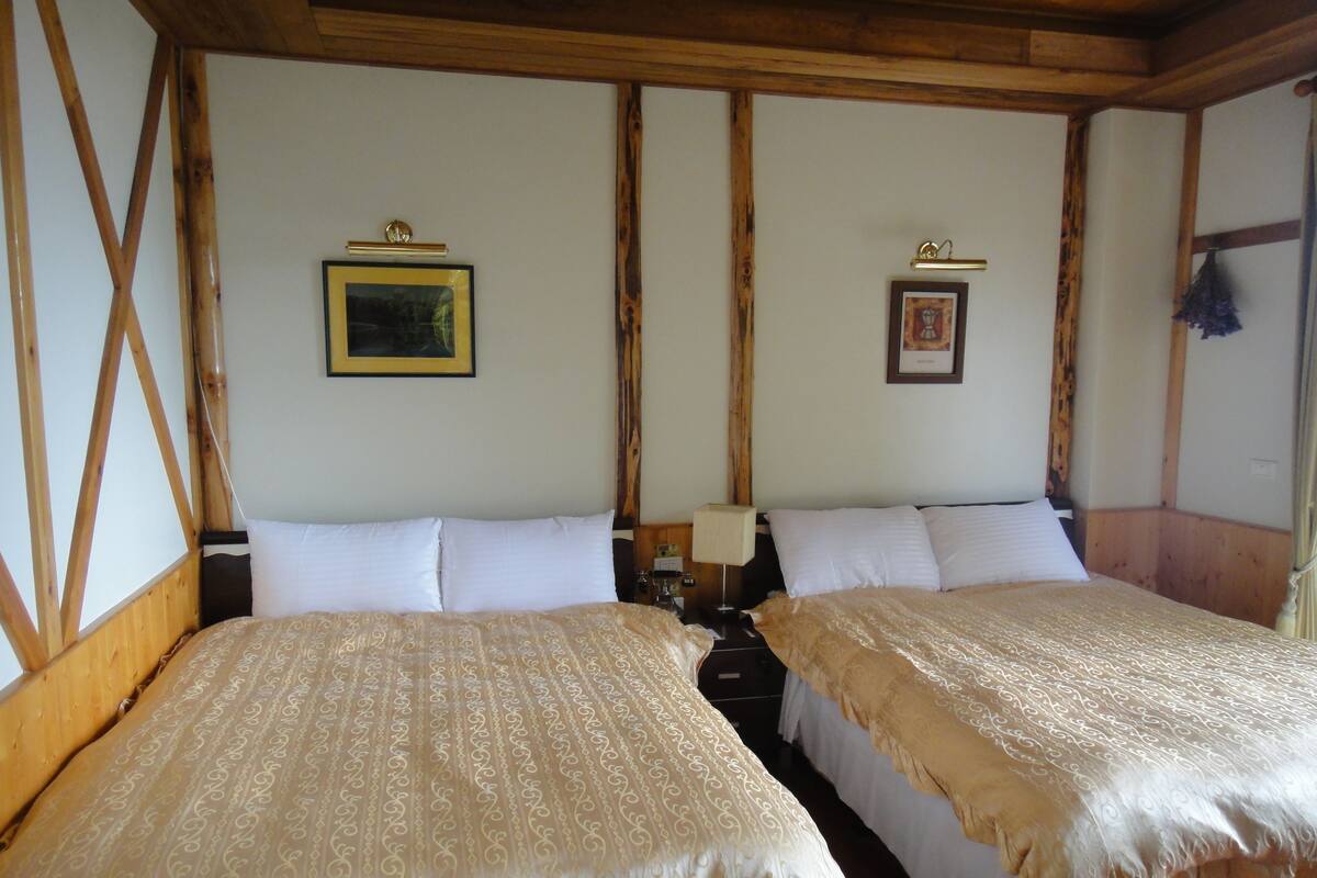 Una habitación con dos camas, vigas de madera, cuadros enmarcados en la pared y techo de madera.