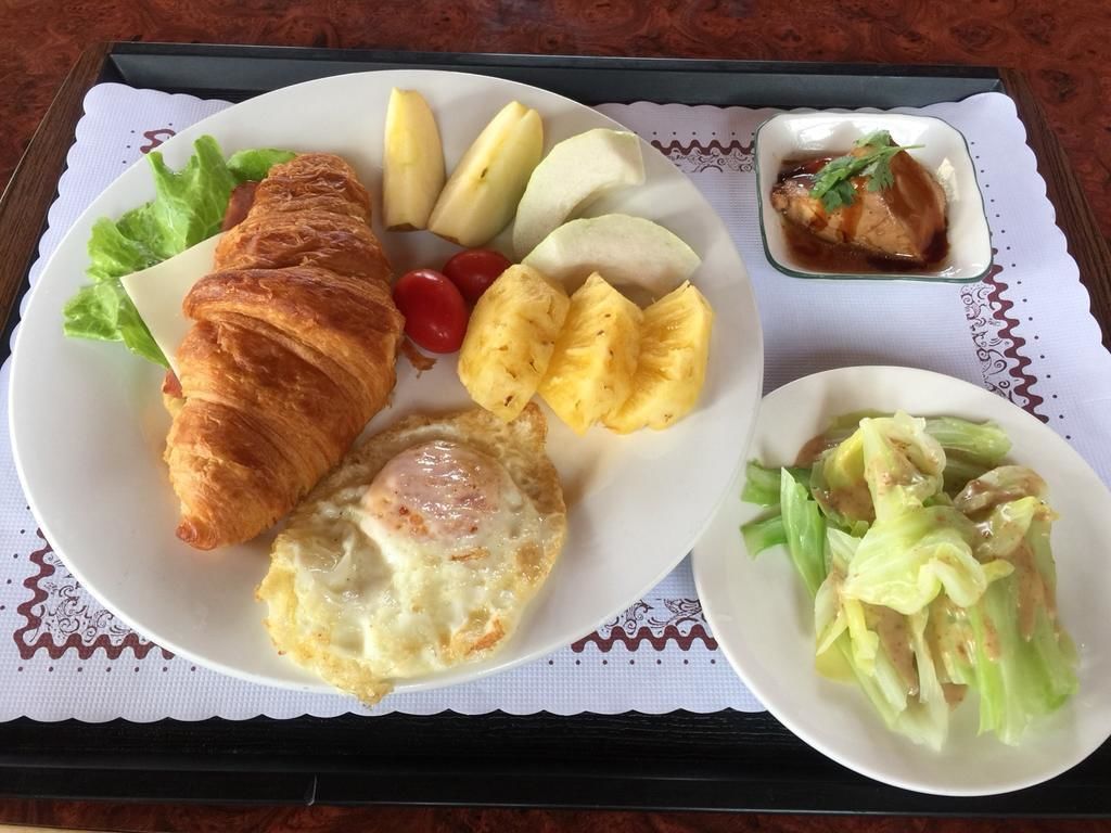 Aamiaistarjotin, jossa on croissant, kananmuna, ananas, tomaatteja ja pieni kulho kastiketta.