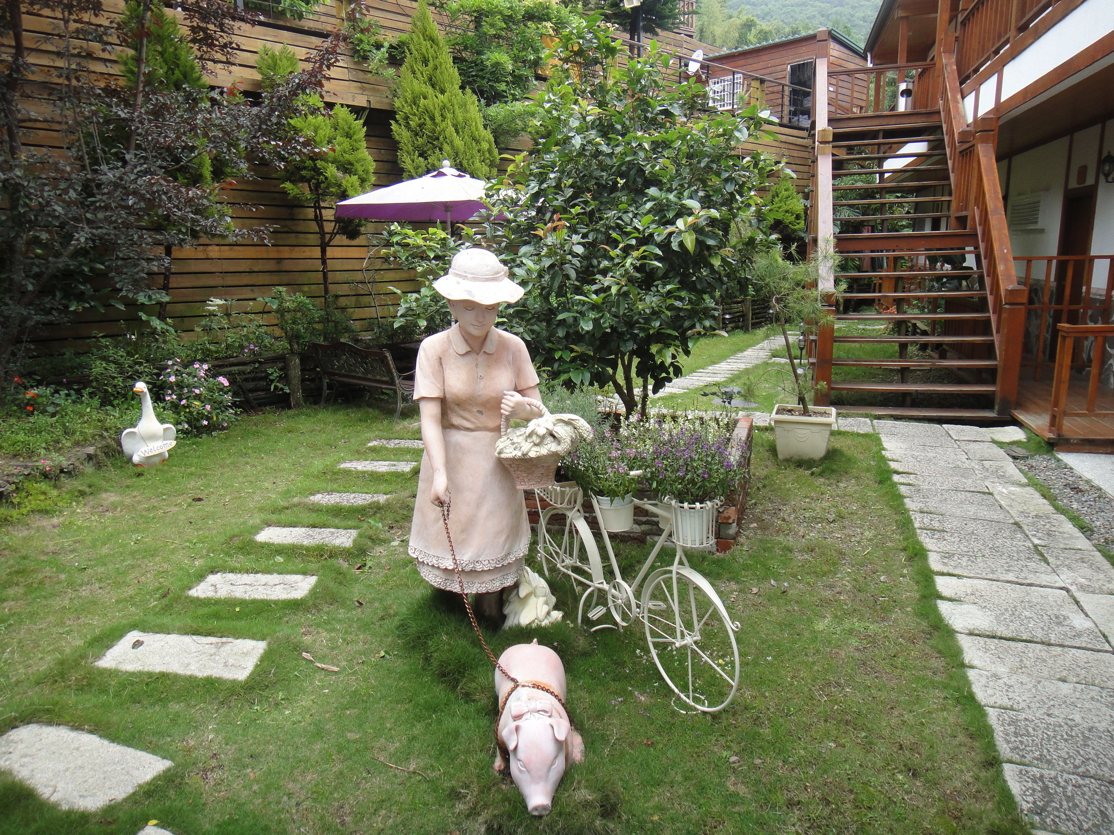 Un jardín con una estatua de una mujer sosteniendo una cesta, un perro y una bicicleta.