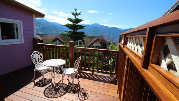 A wooden deck with a table and chairs, a wooden railing, and a view of mountains. - Vienna B and B (Ren'ai)