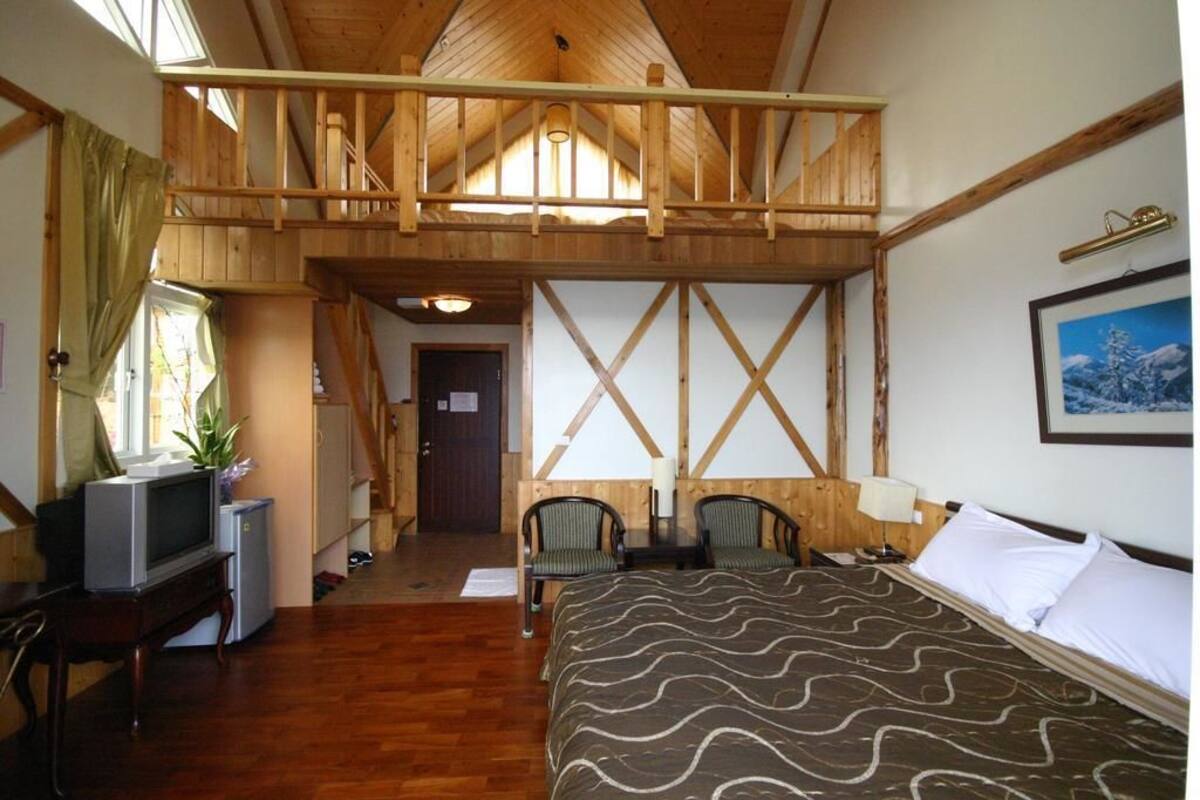 Una habitación con cama alta, vigas de madera, televisor y un escritorio pequeño.