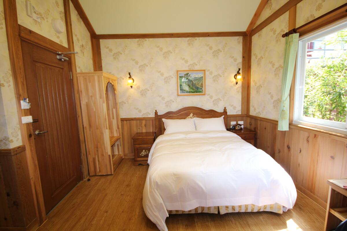 Un dormitorio con cama de madera, mesita de noche, armario y ventana con vistas a zonas verdes.