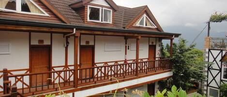 Una casa de madera de dos pisos con un balcón, una valla de madera y vistas al follaje circundante.