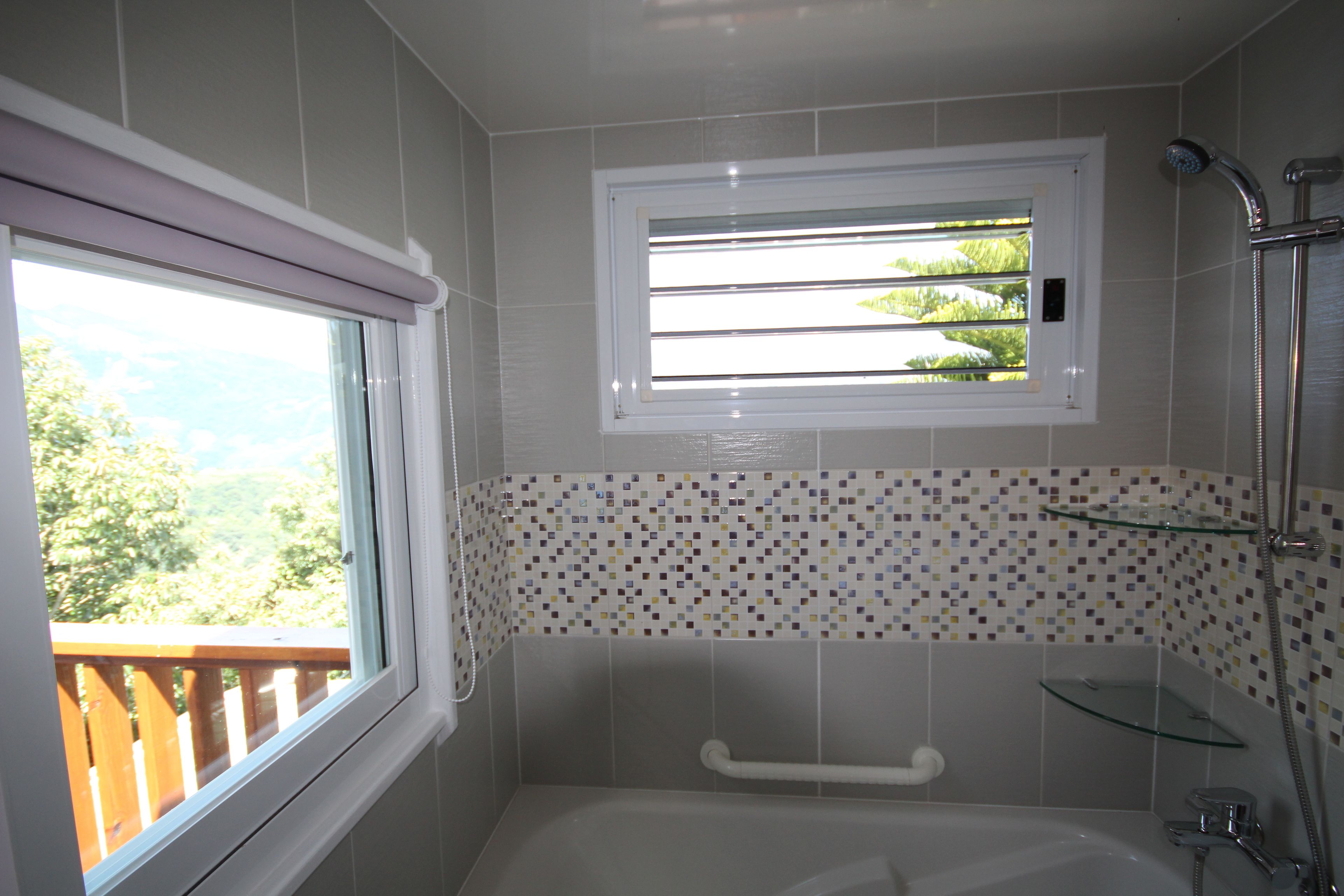 Un baño con bañera, ducha, ventana con persianas y vistas a zonas verdes.