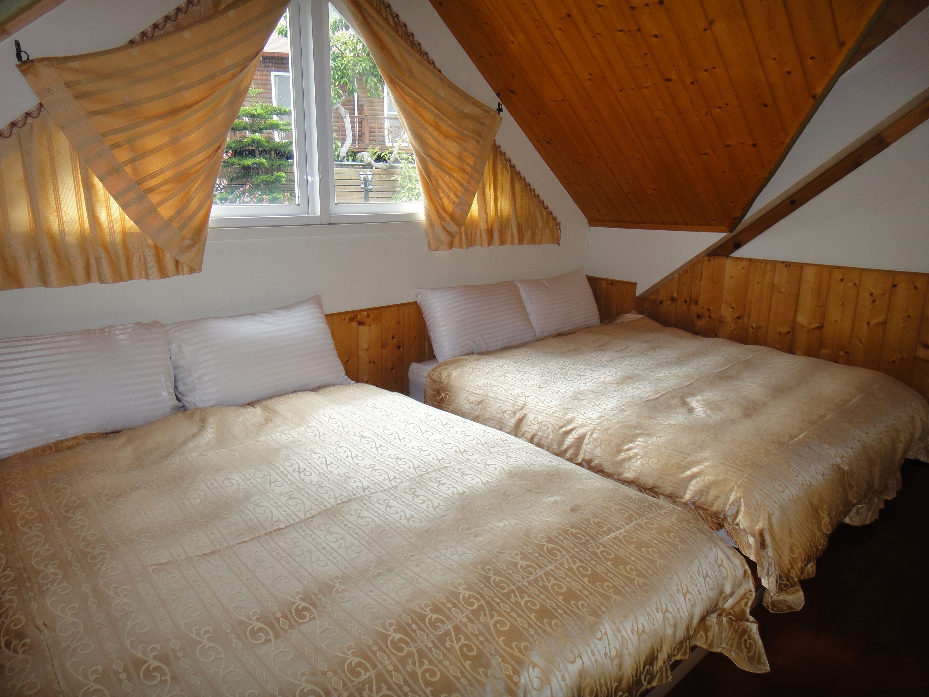 A room with two beds, wooden ceiling beams, and a window with curtains.