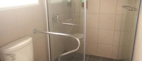 Un baño con ducha de mampara de vidrio, inodoro blanco y paredes con azulejos.