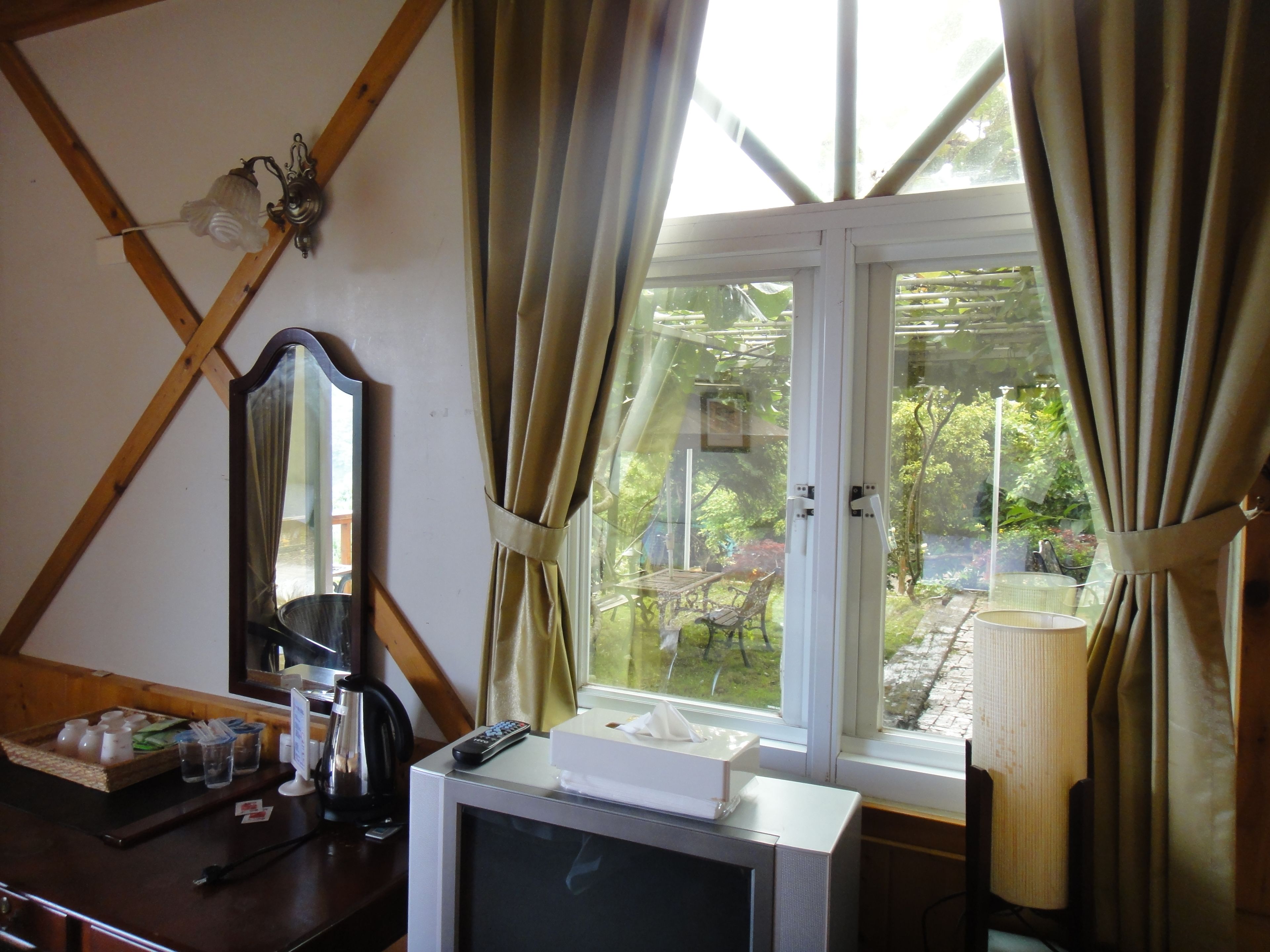 A room with a television, a mirror, and a window with curtains.