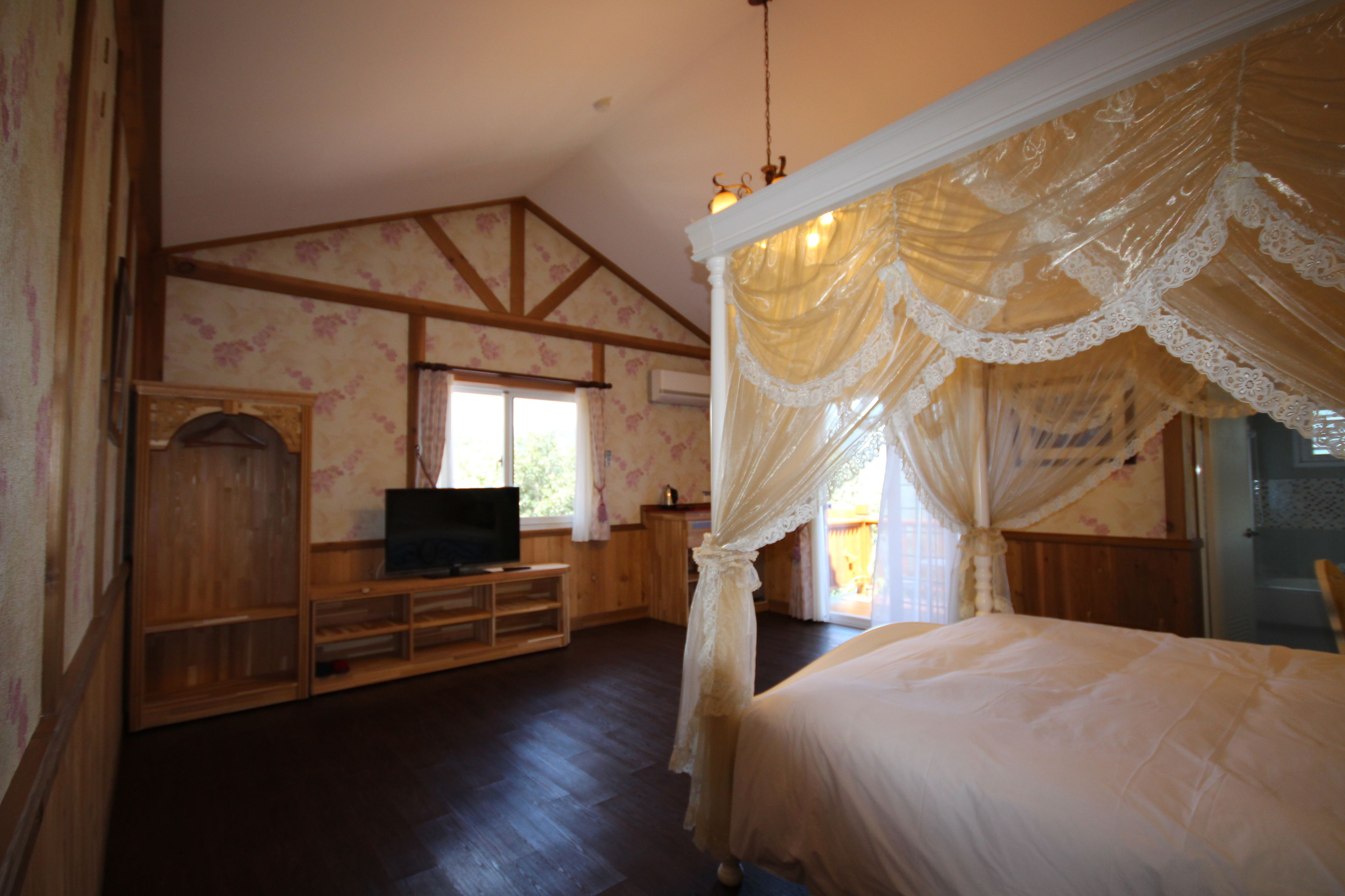 A bedroom with a four-poster bed, wooden furniture, and a television on a wooden stand.