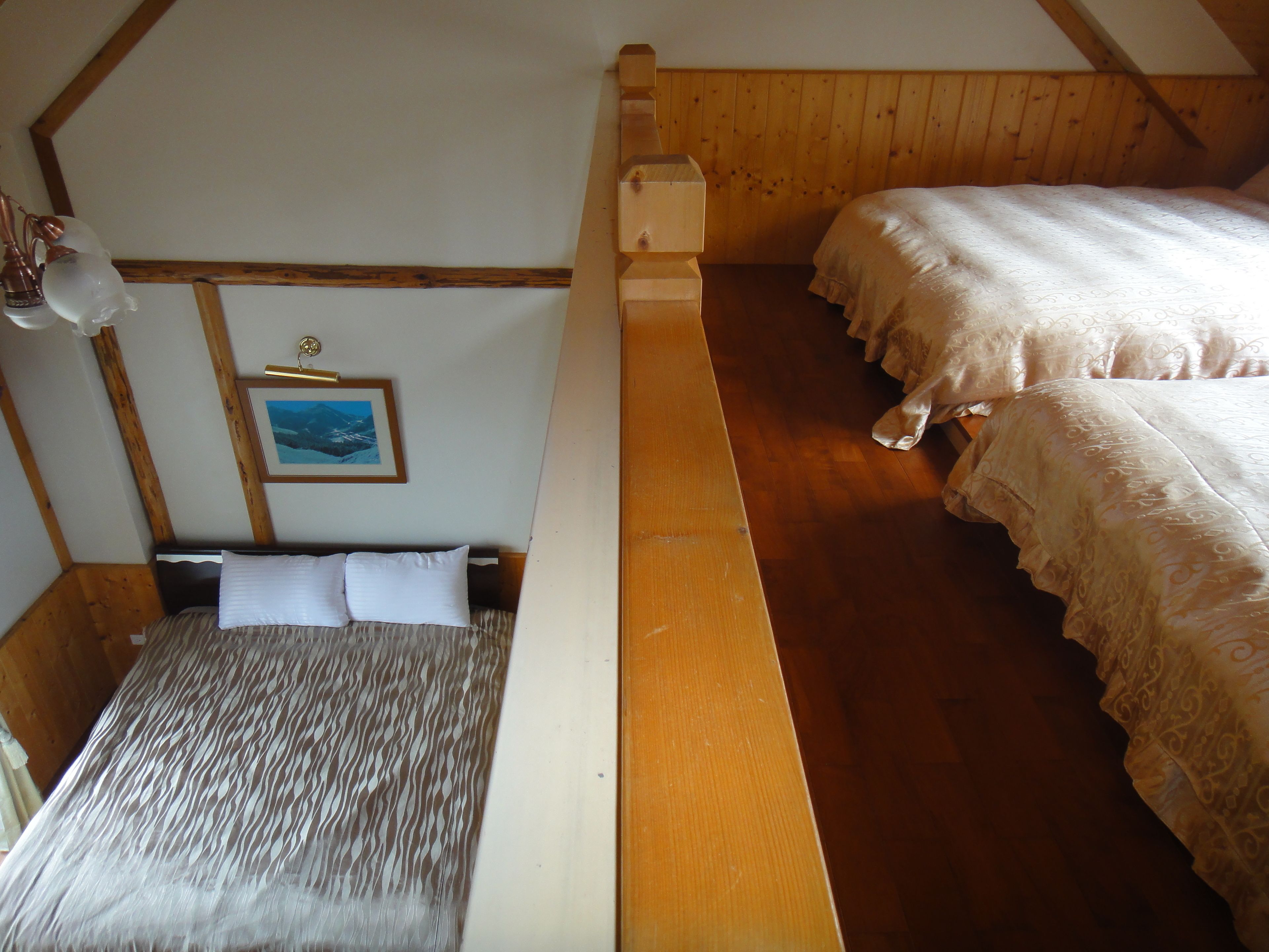 A room with a wooden bunk bed, a single bed with patterned bedding, a framed picture on the wall, and a wooden ceiling.