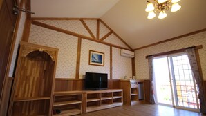 A living room with wooden beams, a television on a wooden stand, a picture on the wall, and a sliding glass door. - Vienna B and B (Ren'ai)