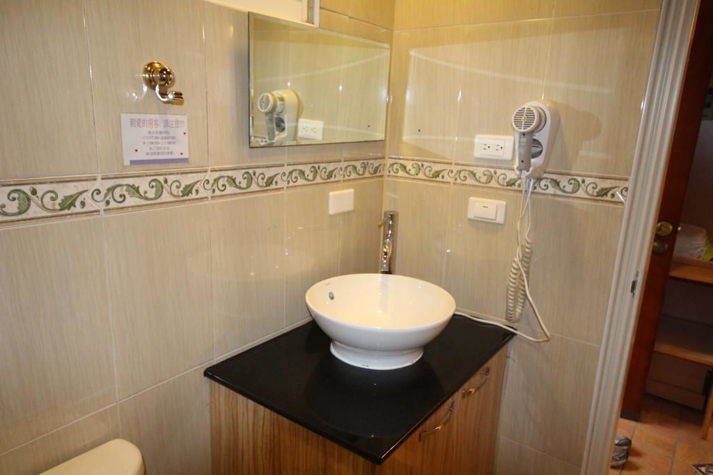 A bathroom with a white sink, black countertop, and a hairdryer on the wall.