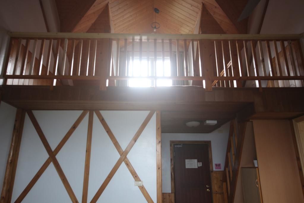 Una habitación con vigas de madera a la vista, techo inclinado y balcón con barandilla.
