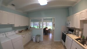 Een keuken met witte kastjes, een magnetron, een fornuis en een eethoek met een tafel en stoelen.
