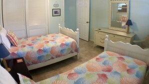 Een slaapkamer met twee eenpersoonsbedden, een plafondventilator, een dressoir en een spiegel.