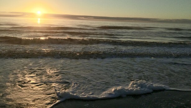 Een strand met golven en de zon die ondergaat.