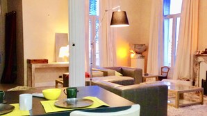 A modern living room with a dining area, featuring a sofa, chairs, a table with a lamp, and a fireplace. - Flat in Beausoleil, Monaco: double glazing, terrace, sea view & paying parking (Beausoleil)
