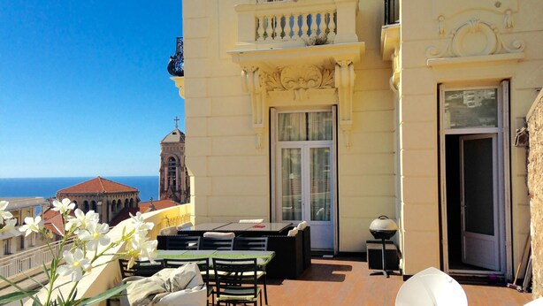 A balcony with outdoor seating, a view of the sea, and a building with classical architecture. - Flat in Beausoleil, Monaco: double glazing, terrace, sea view & paying parking (Beausoleil)