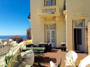 A balcony with outdoor seating, a view of the sea, and a building with classical architecture. - Flat in Beausoleil, Monaco: double glazing, terrace, sea view & paying parking (Beausoleil)