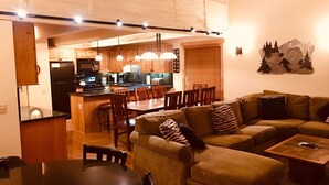 A cozy living room with a sofa, a dining table, and a kitchen area with wooden cabinets and a refrigerator. - Year round fun luxury location steps to Village, close to all outdoor activities (Mammoth Lakes)