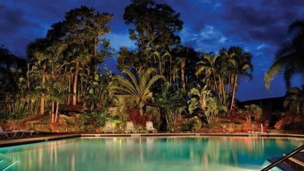 A pool surrounded by tropical vegetation and palm trees at dusk. - Park Shore Resort #355 Lake view, Tennis, Bike/Walk, Gym, Beach, Pickleball (Naples)