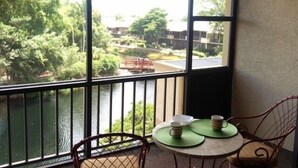 A balcony with a view of a river and greenery, a table with a chair, and a small dining area. - Park Shore Resort #355 Lake view, Tennis, Bike/Walk, Gym, Beach, Pickleball (Naples)