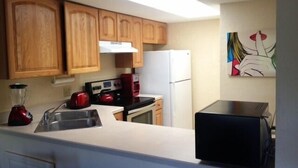 A kitchen with wooden cabinets, a white refrigerator, a red kettle, and a coffee maker. - Park Shore Resort #355 Lake view, Tennis, Bike/Walk, Gym, Beach, Pickleball (Naples)