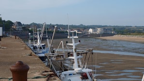 A harbor with several boats docked along the shore, a sandy beach in the background, and buildings across the water. - the charm of Normandy between sea and countryside (Les Moitiers-D'allonne)