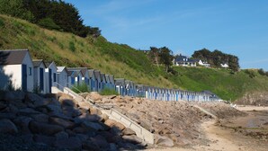 A row of beach huts on a rocky beach with a hillside in the background. - the charm of Normandy between sea and countryside (Les Moitiers-D'allonne)