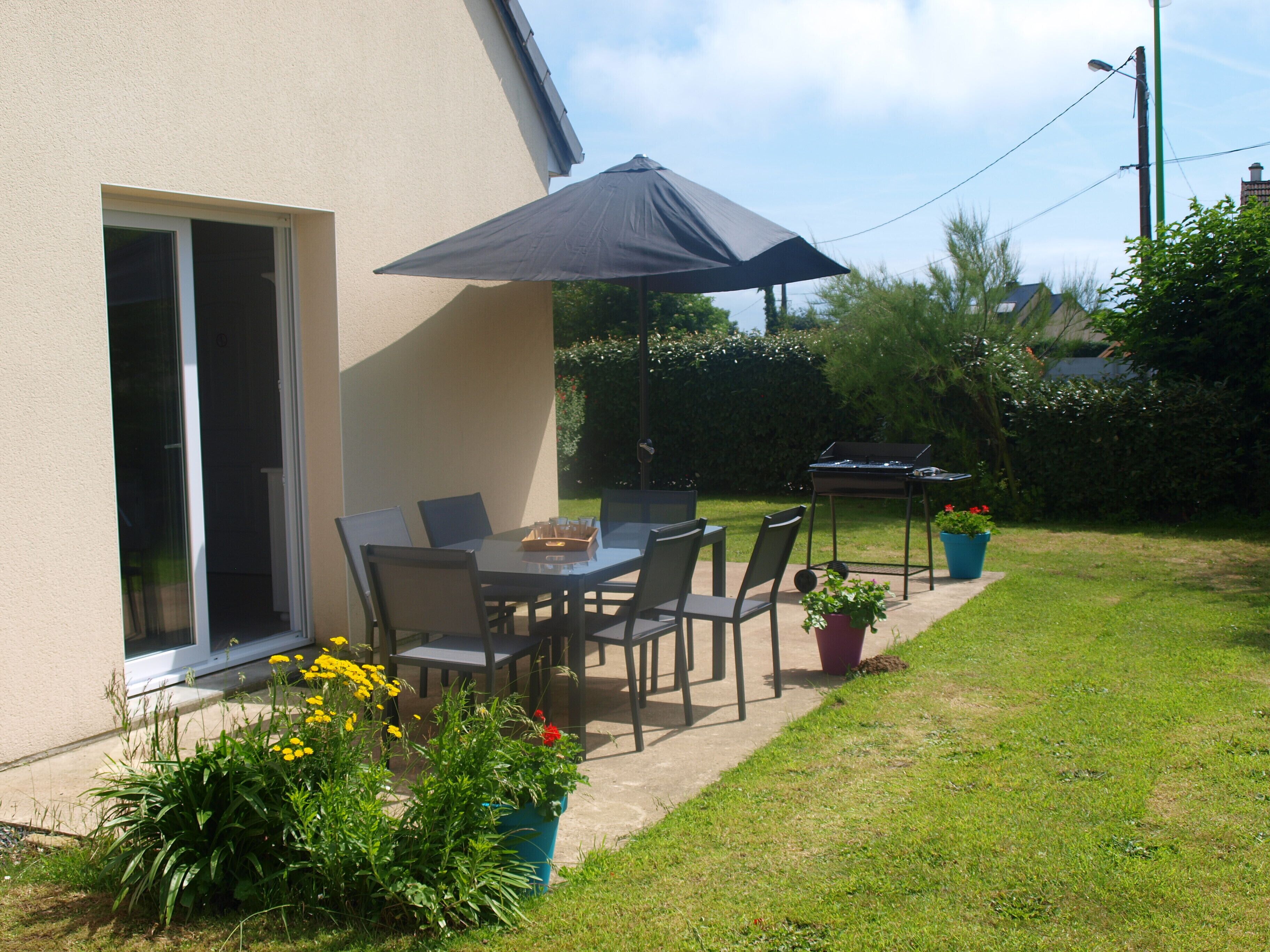 Un patio al aire libre con una mesa, sillas, una parrilla y plantas en macetas.
