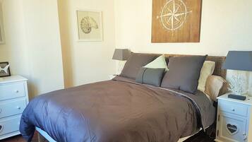 A neatly made bed with a brown bedspread, two bedside tables with lamps, a wall clock, and a framed compass artwork.