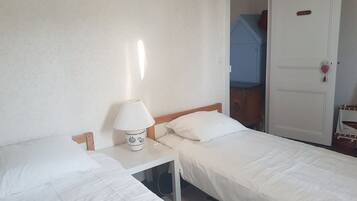Een kamer met twee eenpersoonsbedden, een nachtkastje met lamp en een kledingkast met een hartvormige decoratie.