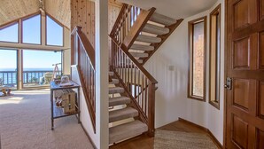 A wooden staircase with a carpeted landing, a wooden door, and large windows offering a view of the outdoors. - Panoramic Views From This Monthly Rental in Cambria! Stunning! (Cambria)